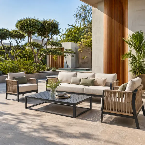 A modern wicker patio sofa set with beige cushions placed in a bright, sunlit commercial outdoor space.