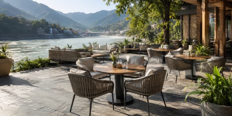 Cozy outdoor patio furniture arranged near a wide river and mountains for riverside resorts.